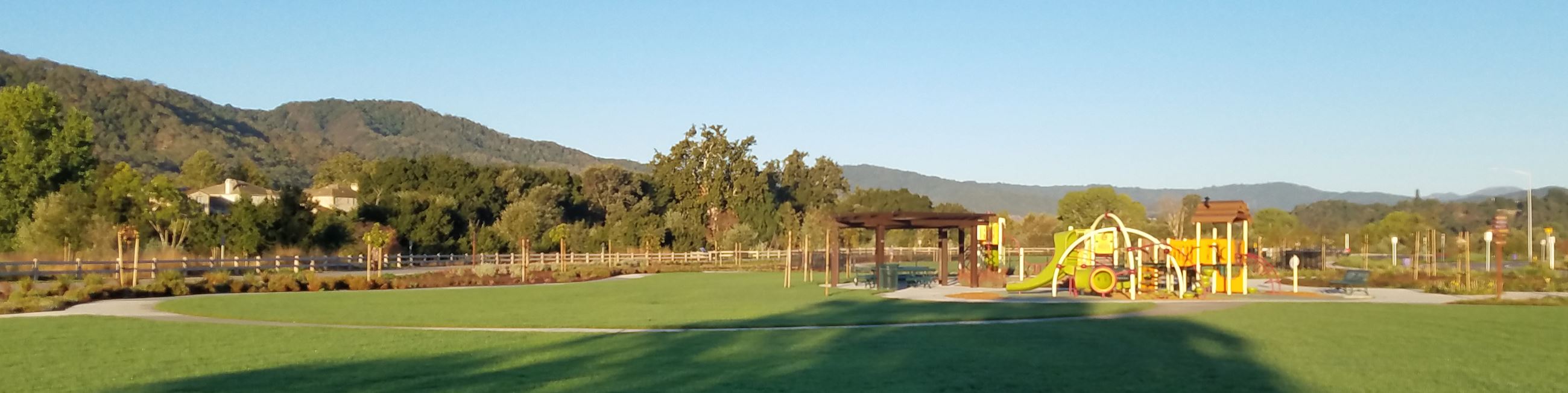 Wide view of Hecker Pass Park showing open lawn, playground, picnic shelter, and surrounding hills 