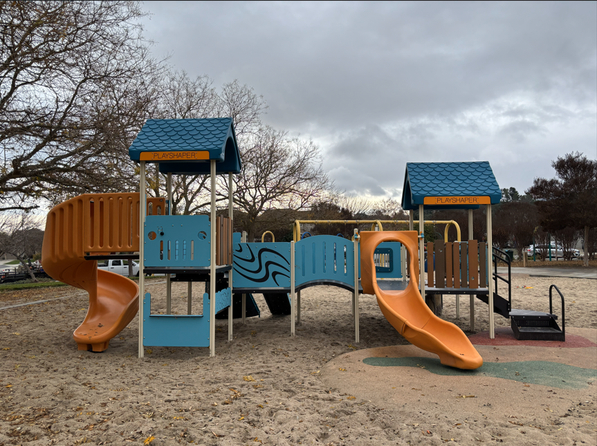 Playground with slides, climbing structures, and sand play area under overcast skies.