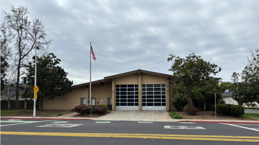 Front view of a Gilroy fire station with two vehicle bays, an American flag, and a street 