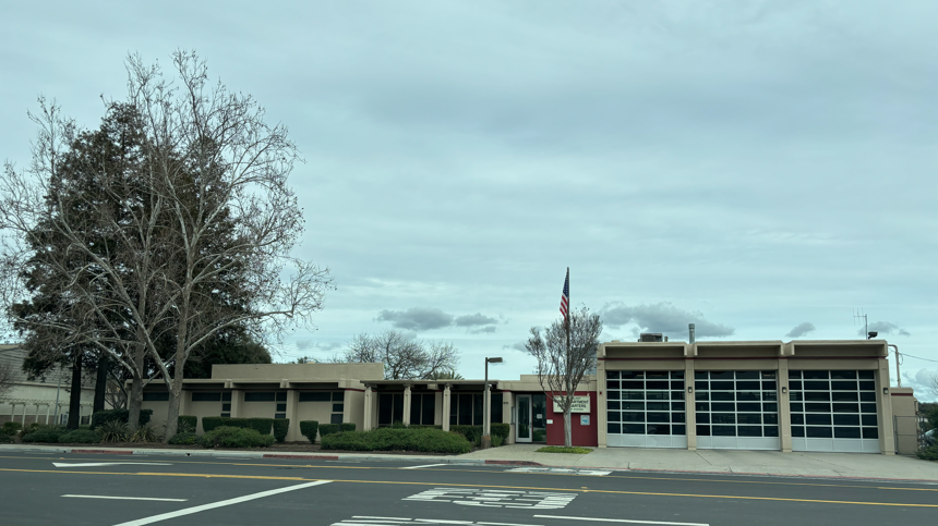 Side view of a Gilroy fire station showing vehicle bays, adjacent building sections, and a street