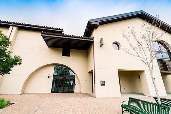 Front entrance of the Gilroy Library featuring an arched doorway, beige exterior walls, and a bench